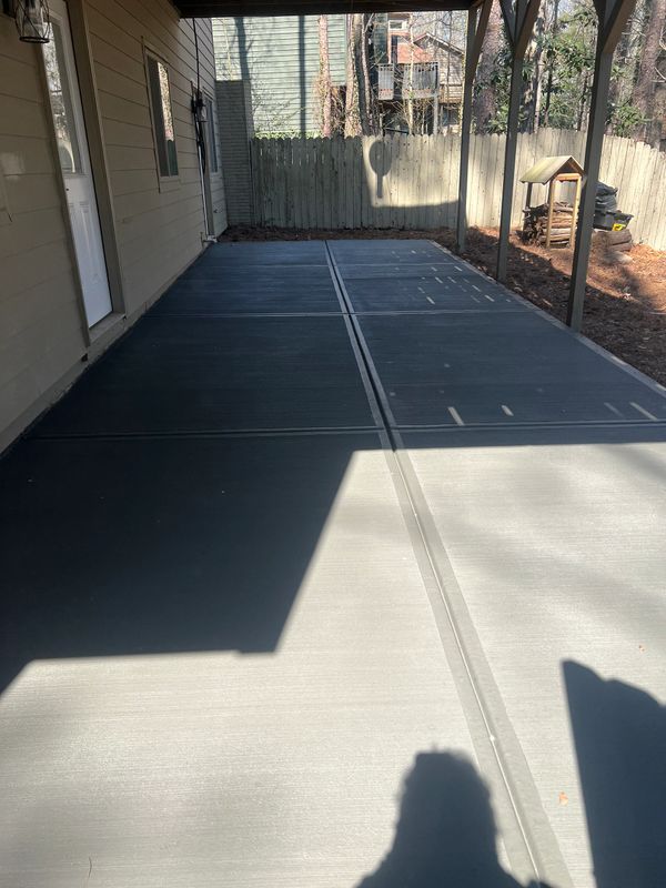 A partially shaded concrete patio under a covered porch with a wooden fence in the background.