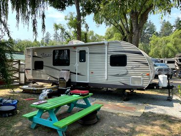 Travel trailer parked under trees with a colorful picnic table nearby.