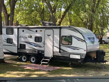 Parked Salem Cruise Lite RV under trees with a patterned outdoor rug.