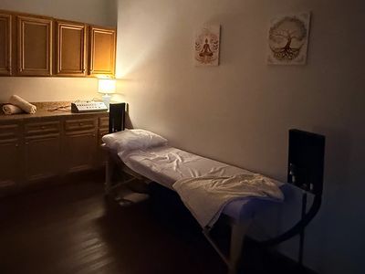 Dimly lit massage or therapy room with a treatment table and warm lighting.