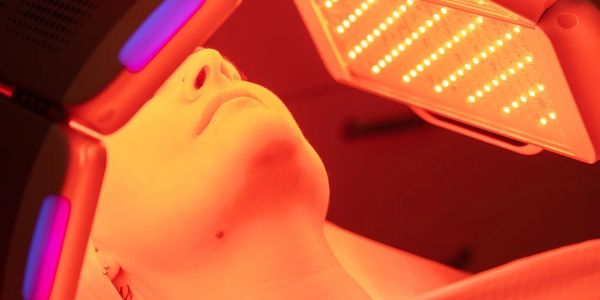 Person undergoing red light therapy on their face under a specialized device.