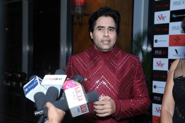 Man in a red sequined jacket speaking to the media at an event.