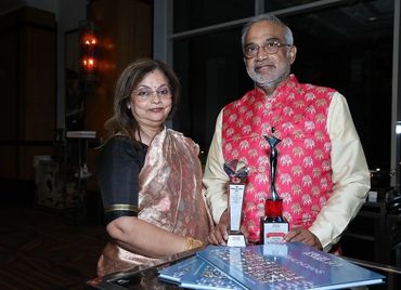 A couple poses with awards and documents, dressed in traditional attire.