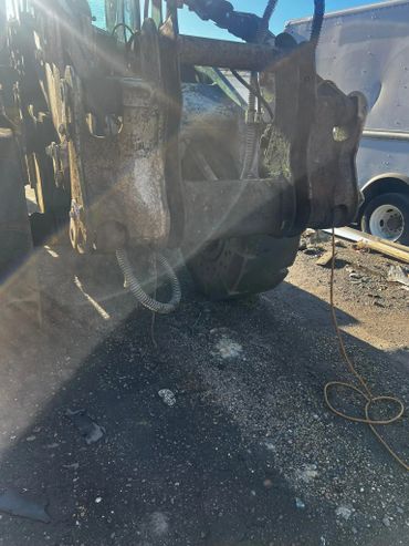 Close-up of a heavy machinery attachment with sunlight glare and industrial surroundings.