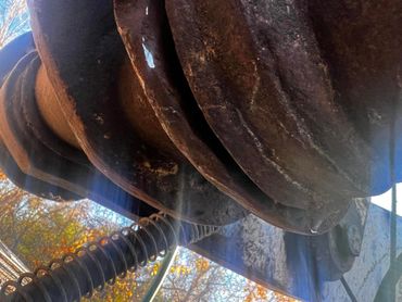 Close-up of a rusted metal spring and large gear outdoors.