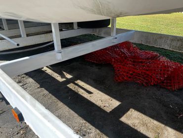 White boat trailer with orange safety reflector and red mesh under it.