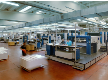 Busy printing factory with workers and large machinery in operation.