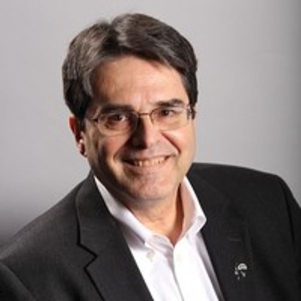 A middle-aged man in a black suit and glasses smiling at the camera.