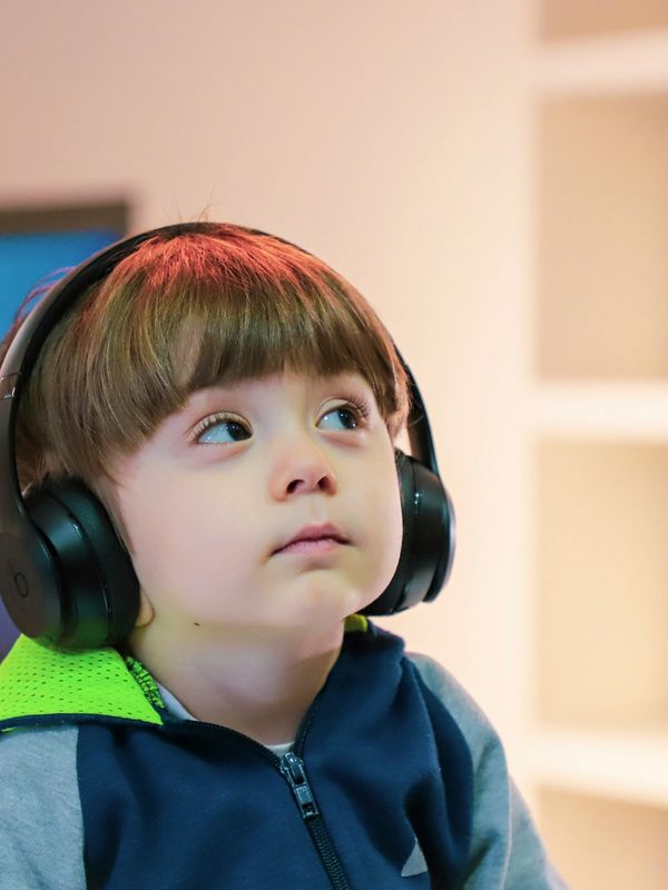 A young boy wearing headphones looks upward thoughtfully.