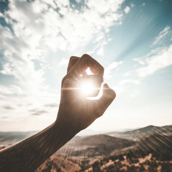 a hand holding holding the sun with valleys and blue sky with clouds