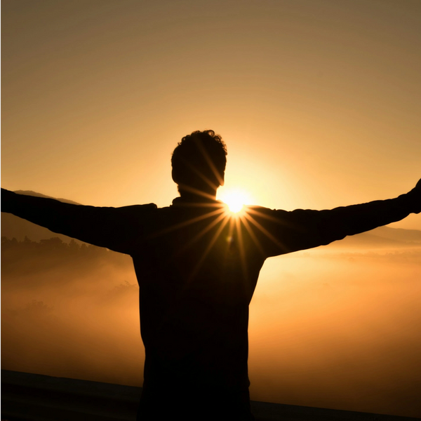 Youth standing on top of a mountain floating and spreading arms being free looking at a sunset