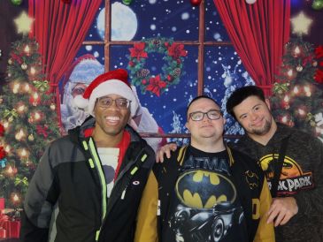 Three friends smiling with Christmas decorations and Santa in the background.