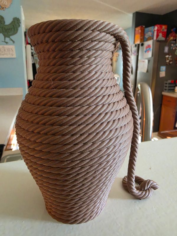 A unique vase made from coiled brown rope on a kitchen counter.