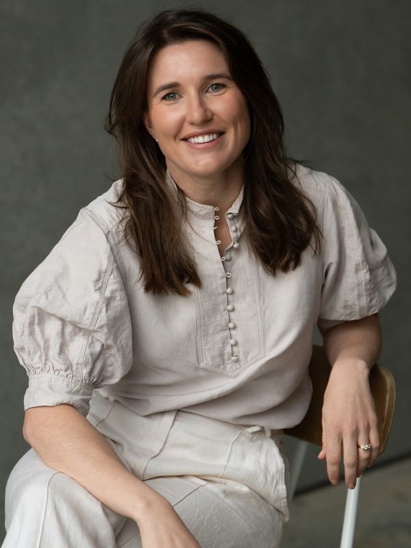 Smiling woman in a white outfit sitting on a chair.