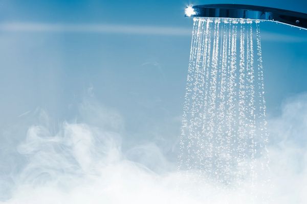 A shiny chrome shower head spraying clear water droplets with steam rising from below.