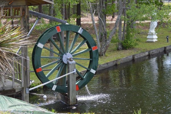 A green wooden water wheel with white and orange accents turning and splashing water into a pond.