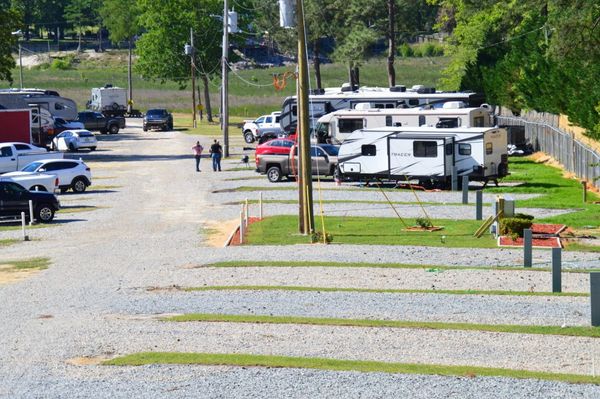An RV park with many parked RVs, travel trailers, and trucks on gravel pads with a dirt road and two