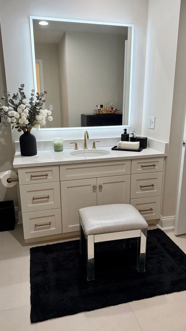 Modern bathroom vanity with illuminated mirror and black cushioned stool.