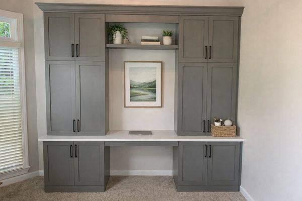 Gray built-in desk with cabinets and a framed landscape picture.