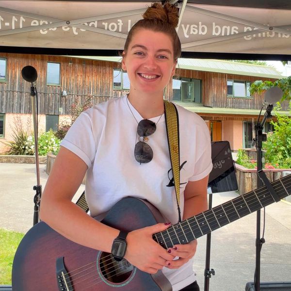 Woman smiling with guitar at outdoor event.