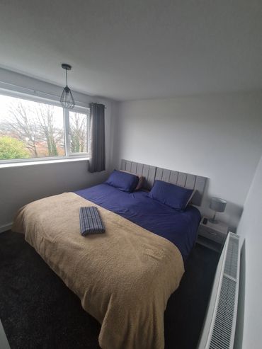 Minimalist bedroom with navy bedding and beige blanket under a window.