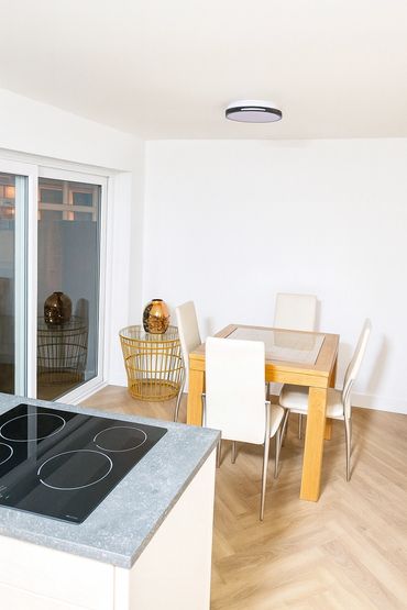 Minimalist dining area with wooden table, white chairs, and modern kitchen counter.