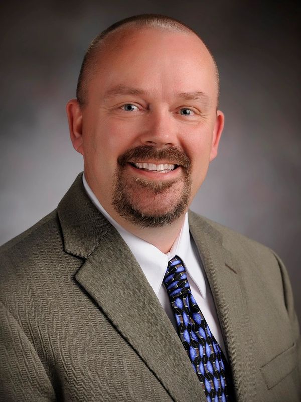 Smiling man in suit and patterned tie against a neutral background.