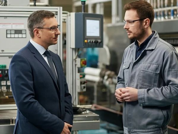 Two men in a factory discussing work near industrial machines.