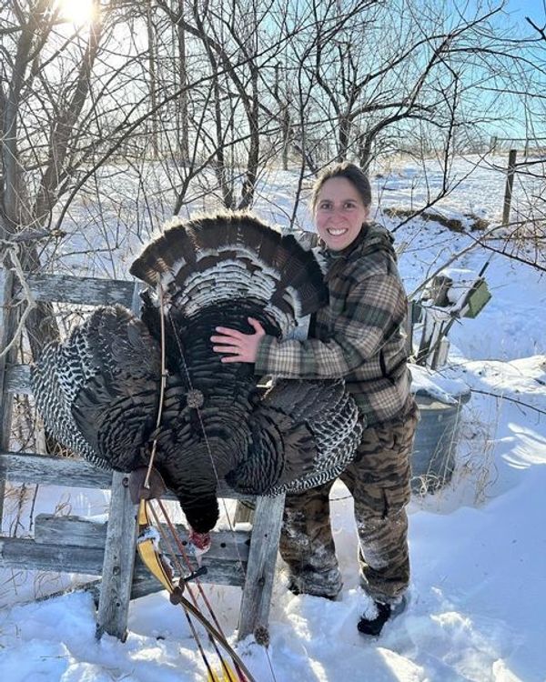 A smiling woman in winter clothes holding a large turkey outdoors in the snow.