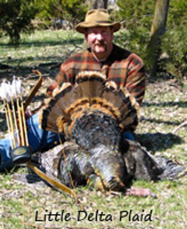 Man proudly holds a large wild turkey he hunted.