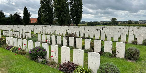 A vast cemetery with rows of white headstones and green grass under a cloudy sky.
