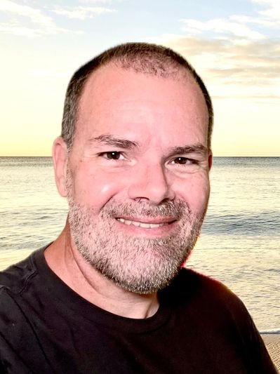 Smiling man with beard by the sea at sunset.