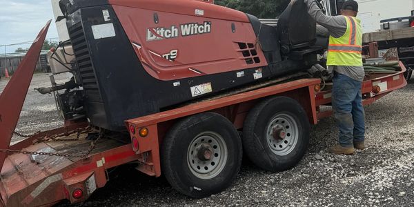 Construction equipment on a trailer with a worker beside it.