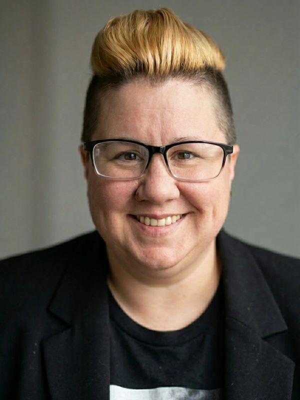 Person with glasses and a smile wearing a black blazer.