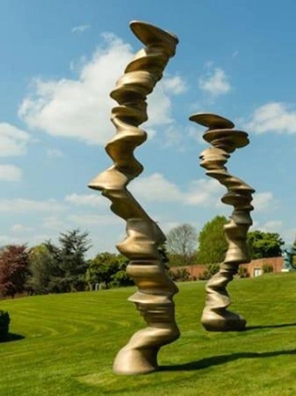 Three abstract twisted bronze sculptures on a green lawn under a blue sky.
