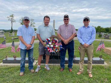Four men standing in a cemetery with American flags and a wreath.