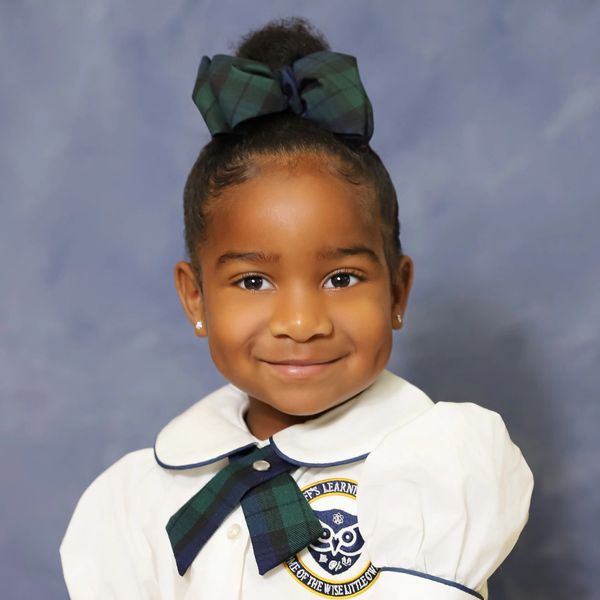 Smiling young girl in school uniform with a bow and emblem.
