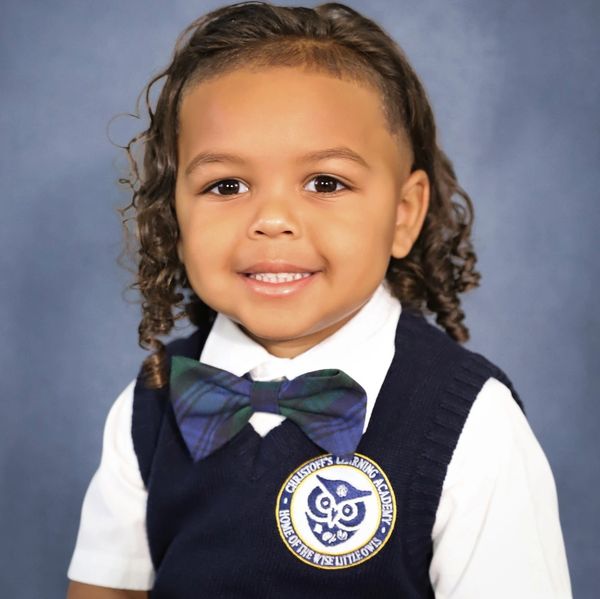 Smiling young boy in school uniform with bow tie and curly hair.