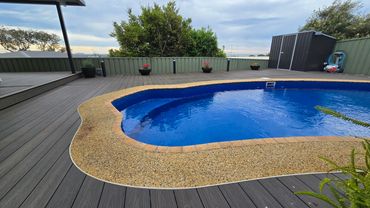 A backyard pool with wooden deck and garden shed under a cloudy sky.