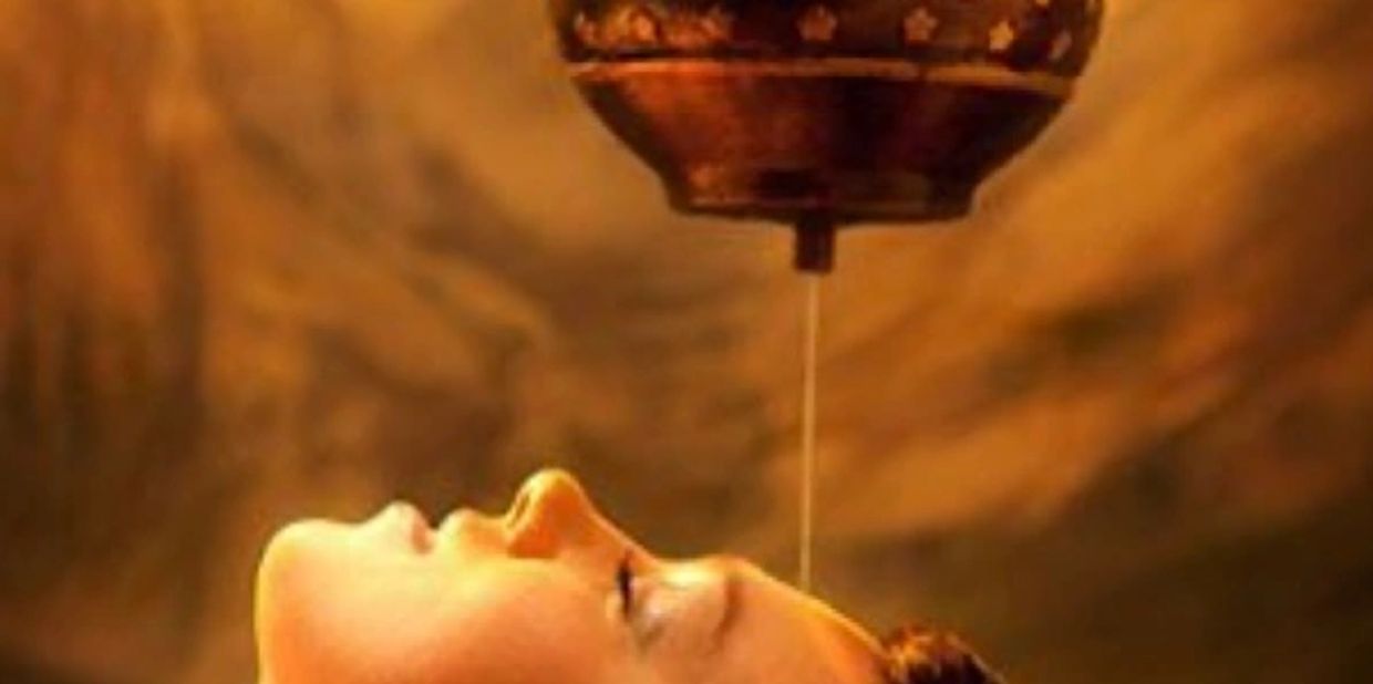 Person receiving traditional Ayurvedic Shirodhara therapy with oil dripping on forehead.