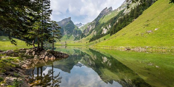 Serene mountain lake reflecting trees and peaks under a blue sky.