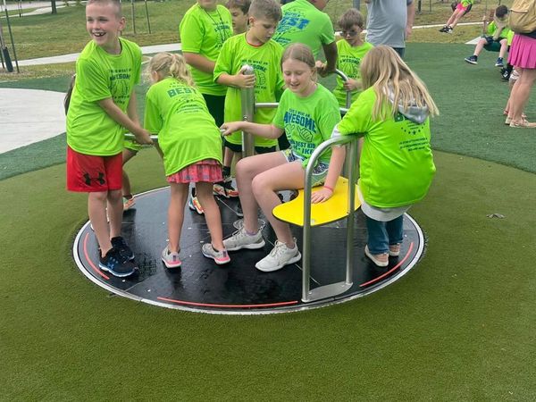 Children playing on a merry-go-round in matching green shirts.