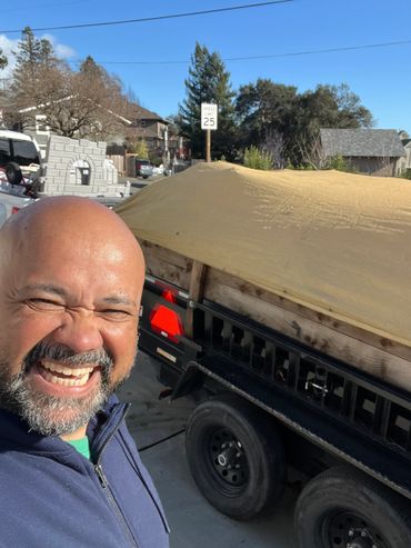 Man smiling beside a covered trailer under clear skies.