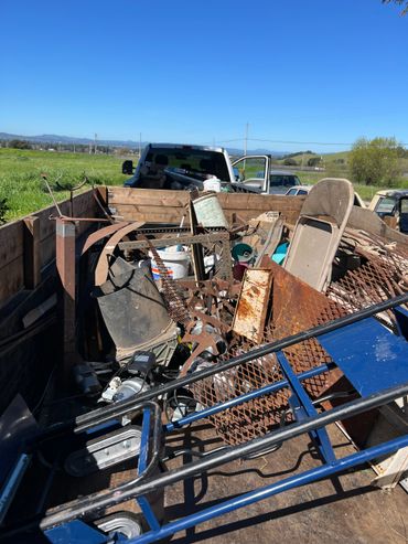 A truck bed filled with various rusty metal scraps, tools, and old equipment under a clear blue sky.