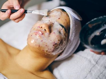 A woman is having a facial mask applied with a brush at a spa.