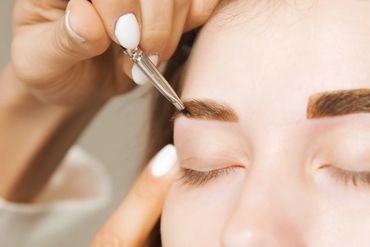 Close-up of eyebrow makeup application with a brush on closed eyes.