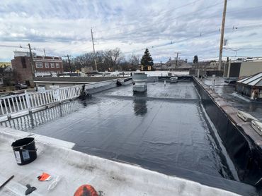 Newly sealed flat roof with wet black coating on a cloudy day.