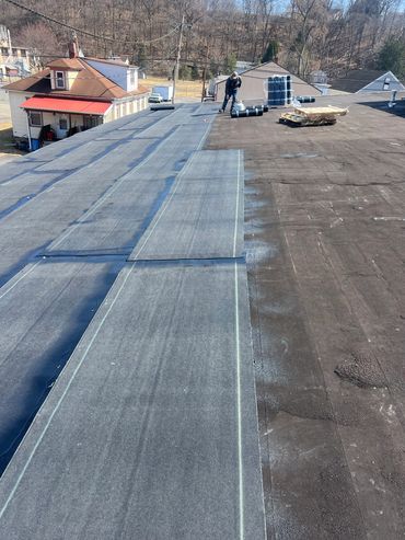 Worker installing waterproof membrane on a flat roof under clear skies.