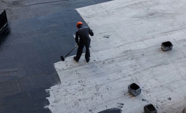 Worker applying black coating on a large white surface with a roller.