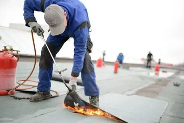 Worker using a blowtorch to install roofing material.
